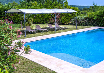 Piscine avec transats à côté, protégés par une structure, et entourée de nature verdoyant