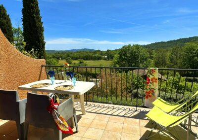 Terrasse avec table dressée, deux chaises et transats, offrant une vue dégagée sur les vignobles environnants