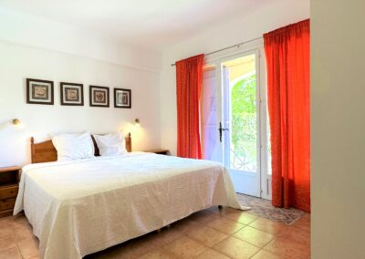 Chambre d'un appartement avec lit double aux draps blancs et rideaux oranges, offrant un décor élégant et confortable