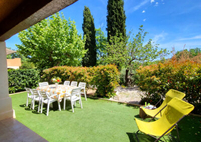 Terrasse avec une partie couverte et une section extérieur, semblable à un jardin, comprenant une table à manger et deux transats. La terrasse est entourée de verdure luxuriante