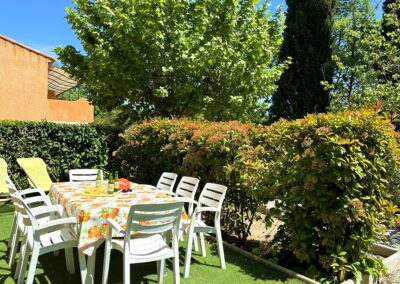 Sur la terrasse au rez-de-chaussée, entourée par la verdure, une table à manger avec apéritif et deux transats pour se détendre